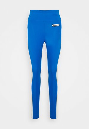 Zilas legingi ar augstu jostasvietu un melnu Adidas logotipa uzšuvumu. Iezīmēti ar kontrastējošām baltām sānu svītrām. Gluda, elastīga auduma konstrukcija.