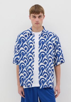 Chemise à manches courtes avec un motif bleu et blanc tournant, dotée d'un devant boutonné et d'une coupe décontractée, associée à un t-shirt blanc uni.