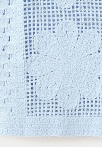 Tissu crocheté bleu clair avec un motif floral et un fond en forme de grille, avec des pétales en spirale détaillés et une bordure texturée.