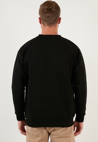 Hanorac negru, cu guler rotund, manșete și tiv cu nervuri, fabricat dintr-un material moale. Design simplu, fără logo-uri sau modele vizibile pe spate.