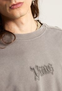 Šedá mikina s kulatým výstřihem a žebrovaným lemem. Na přední straně se nachází temný, stylizovaný logo "Vans". Měkká, mírně strukturovaná tkanina.