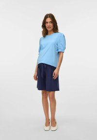 Gaiši zils īsām piedurknēm tops ar pūkainiem pleciem, apvienots ar tumši ziliem šortiem ar sasietu jostu, izgatavots no mīksta auduma un vienkāršā dizainā.