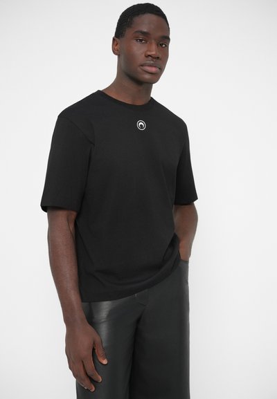 Juoda medvilninė marškinėliai trumpomis rankovėmis ir apvalia apykakle, su apskritu baltu logotipo akcentu ant krūtinės.