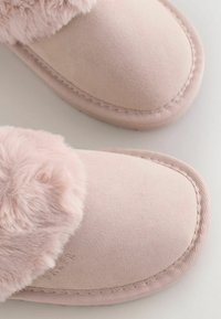 Pantofole rosa con una morbida tomaia in suede, trim in pelliccia sintetica e dettagli cuciti lungo il bordo. Forma a punta rotonda con una texture liscia.
