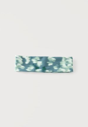 Bandeau en tissu tie-dye bleu et blanc avec une texture douce et extensible, posé à plat sur un fond clair uni.