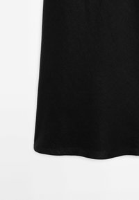 Tissu noir avec un motif texturé subtil qui tombe en douceur, montrant le bord inférieur d'un vêtement sur un fond blanc.