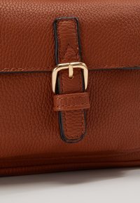 Sac en cuir marron texturé avec une boucle en métal doré et un détail de sangle cousue sur une surface claire.
