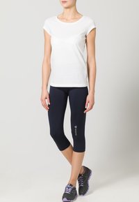 Vit t-shirt med kort ärm i kombination med marinblå capribyxor. Svarta träningsskor med lila accenter. Enkelt, figurnära design och mjuk textur.