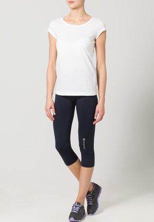 T-shirt bianco a maniche corte abbinato a leggings capri blu navy. Scarpe da ginnastica nere con dettagli viola. Design semplice e aderente, con una texture morbida.