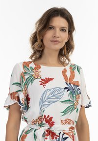 Bloemenjurk met een witte achtergrond, voorzien van kleurrijke bladeren en bloemen in rood, groen en blauw. Inclusief volants mouwen en een vanille taille.