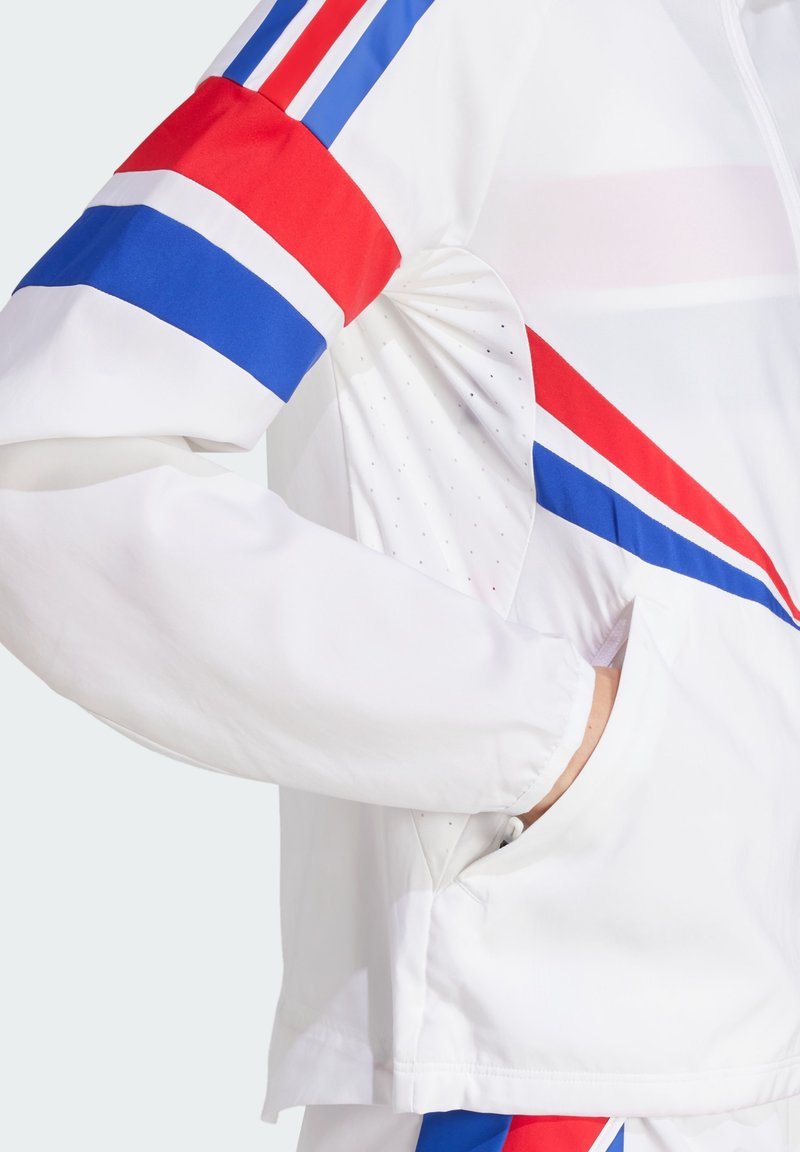 Chaqueta deportiva blanca con rayas rojas, azules y blancas en las mangas. Incluye un diseño texturizado con detalles perforados.
