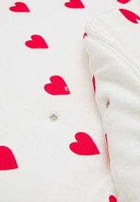 White fabric with scattered red hearts pattern and a zippered edge. Includes a metal snap. Soft texture.