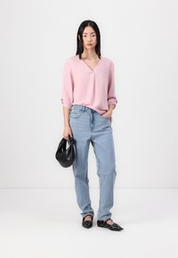 Lys rosa v-hals bluse med trekvart ermer, kombinert med lys blå høytlivsjeans. Svart håndveske og flate sko med hullmønster.