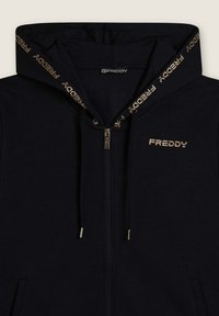 Felpa nera con zip, caratterizzata da un logo con accenti dorati e lacci, con una texture morbida e un cappuccio foderato in nastro brandizzato.