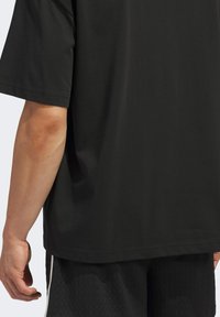 Černá košile s krátkým rukávem a volným střihem. Tkanina vypadá hladce s mírným leskem, má čistý a minimalistický design.