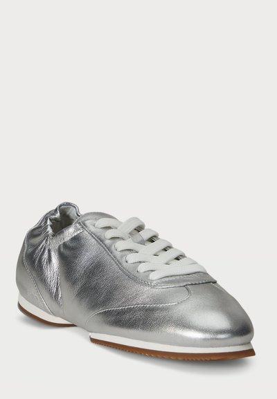 Silverfärgade metalliska sneakers med rund tå, snörning i vit textil och en flexibel, ljusbrun gummisula. Slät yta genom hela skon.
