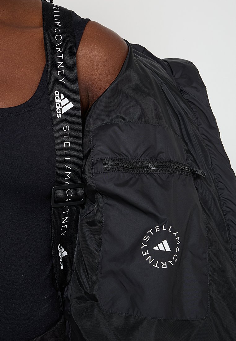 Czarna kurtka puchowa z zamkiem błyskawicznym i okrągłym logo. Posiada markowy pasek z napisem "STELLA McCARTNEY" i "adidas". Gładka tekstura.