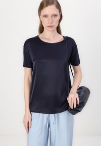 Top corto a maniche corte di color blu navy con scollo rotondo, realizzato in tessuto morbido. Abbinato a pantaloni blu chiaro e una borsa scura tenuta nella mano destra.