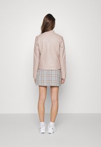 Giacca in pelle rosa chiaro con design aderente, colletto piegato e maniche lunghe, abbinata a una minigonna a quadri e sneakers bianche.