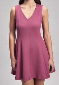 Robe sans manches à décolleté en V en tissu texturé de couleur rose moyen. Jupe évasée avec un corsage ajusté. Se termine au-dessus du genou. Détails de couture à l'avant.