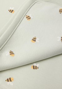 Lys grøn stof med en blød tekstur, prydet med små broderede bier i gult og sort med hvide vinger, der er jævnt fordelt over materialet.