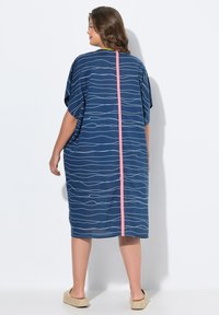 Kaftan bleu avec des motifs blancs ondulés, une rayure verticale rose au dos, des manches courtes et une coupe ample et décontractée.