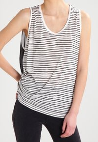 Canotta a righe bianco e nero con scollo rotondo, vestibilità ampia e tessuto morbido. Presenta un leggero drappeggio e un design del retro a contrasto.