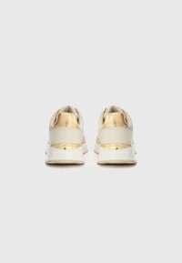 Lys beige sneakers med en teksturert overdel, gullfargede detaljer på hælen, og en hvit såle. Rund design med polstret bak.