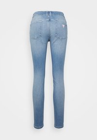 Jeans ajustados en denim azul claro. Presenta una cintura alta, cinco bolsillos y un pequeño logo de la marca en el bolsillo trasero. Textura suave.