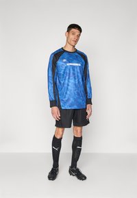 Sinine ja must pika varrukaga jersei, millel on kamuflaažimuster, sisaldab "UMBRO" logo. Kombineeritud mustade lühikeste pükste ja mustade sokkidega, millel on valged aktsendid.