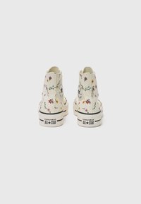 Vita canvas högsko-sneakers med blommönster, en gummisula och svarta detaljer samt Converse All Star-logotypen på hälen.