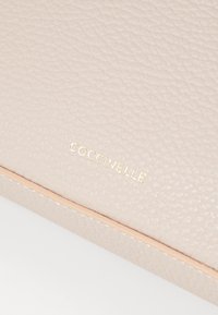 Borsa a mano in pelle texture rosa chiaro con impresso in oro il marchio, caratterizzata da dettagli con bordi lisci e un sottile motivo a grana.