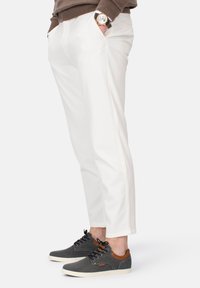 Weiße, schmal geschnittene Hose mit glatter Textur. Kombiniert mit dunkelgrauen Sneakers mit braunen Akzenten und weißer Sohle. Sichtbare Detailnähte.