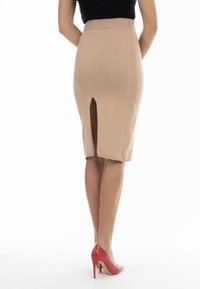 Beige Bleistiftrock in knielanger Länge aus dehnbarem Material mit einem Schlitz hinten; kombiniert mit roten High Heels.
