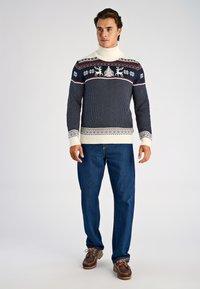 Marinblå tröja med vit polokrage, mönster med renar och snöflingor, strukturerat tyg, kombinerad med blå jeans och bruna skor.