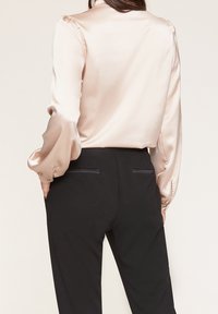 Krämfärgad satinklänning med långa, puffärmar, matchad med höga svarta byxor med diskreta bakfickor och en slät textur.