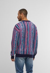 Mehrfarbiger gestrickter Pullover mit einem auffälligen geometrischen Muster in Pink, Blau und Lila; gerippte marineblaue Bündchen und Saum; lockere Passform.