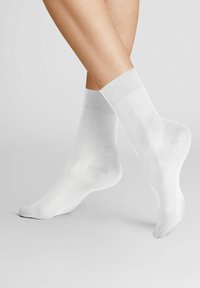 White cotton socks with a smooth texture, a ribbed cuff, and a snug fit. They cover the ankle and feature a seamless toe design.