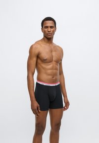 Μαύρα ανδρικά εσώρουχα μποξέρ από βαμβάκι, με γκρι και ροζ ζώνη μέσης που φέρει το λογότυπο της Nike. Το σχέδιο έχει εφαρμοστή γραμμή και ομαλή υφή.