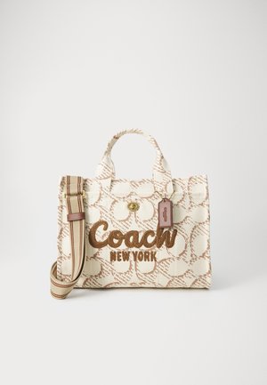 Sac en toile crème avec un motif circulaire marron, présentant un logo "Coach New York" brodé, des poignées doubles et une bandoulière réglable.