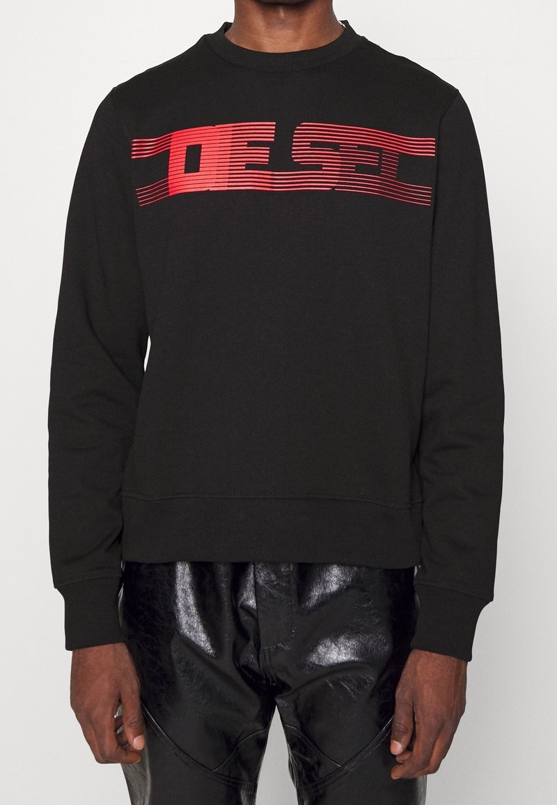 Sweatshirt noir avec texte horizontal rouge au niveau de la poitrine. Design simple à col rond avec manches longues et poignets côtelés.
