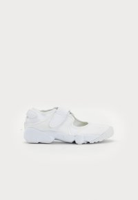 White athletic shoe with a rounded toe, mesh upper, adjustable strap, and textured sole featuring the word "AIR" embossed on the side.