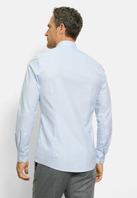 Helleblaue Button-down-Hemd mit langen Ärmeln, subtilen diagonalen Mustern und abgerundetem Saum. Verfügt über einfache weiße Knöpfe und einen klassischen Kragen.
