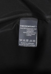 Schwarzer Polyesterstoff mit einem Etikett, das "SWEDEMOUNT™" angibt. Pflegehinweise und Materialdetails in einer klaren, weißen Schrift gedruckt.