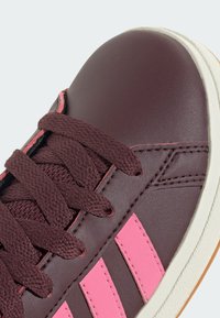 Zapatilla deportiva burdeos con rayas rosas, parte superior texturizada, puntera round y cordones planos. Suela de goma blanca con acabado ligeramente texturizado.