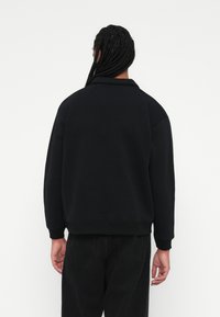 Sudadera negra con dobladillo y puños acanalados, que muestra un ajuste relajado y una textura suave. Estilizada con un cuello y un detalle de costura trasera sencilla.
