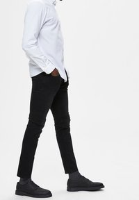 Svarta jeans, vit skjorta med knappar, svarta skor, grå strumpor. Slim fit-design med en slät textur. Skjortan har långa ärmar och en klassisk krage.