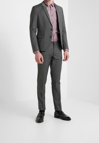 Traje gris a medida con un acabado texturizado, combinado con una camisa de botones color rosa claro y mocasines negros con detalles plateados.