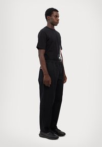 Black t-shirt with a graphic print, paired with black pants featuring an elastic waistband and side pockets. Black sneakers complete the look.