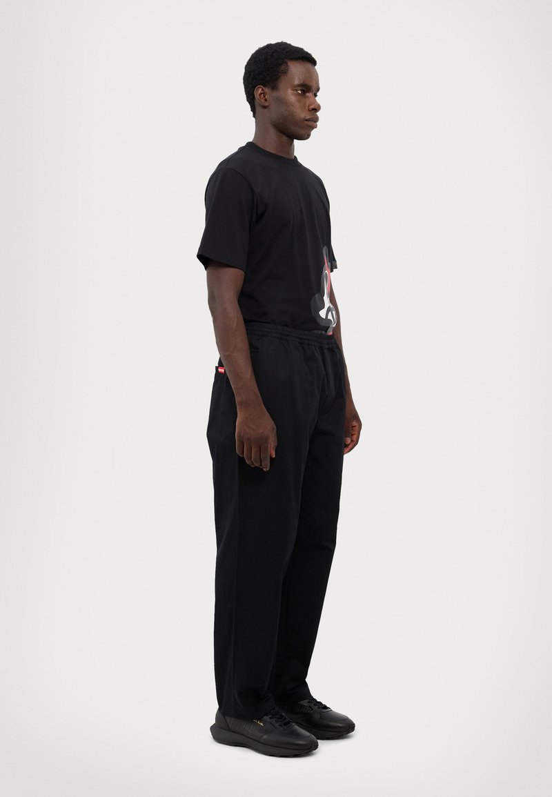 Black t-shirt with a graphic print, paired with black pants featuring an elastic waistband and side pockets. Black sneakers complete the look.